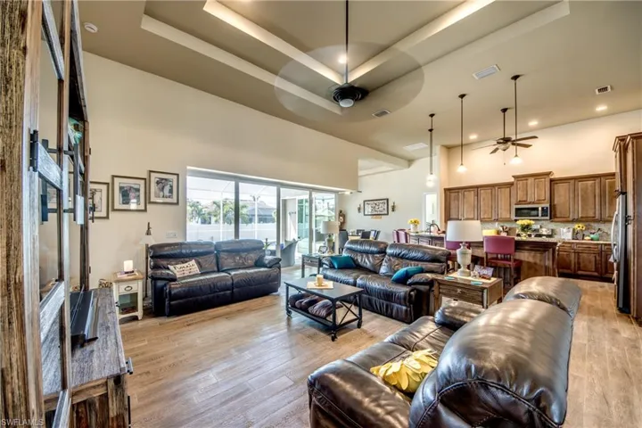 Living room with a tray ceiling, light wood finished floors, a ceiling fan, and recessed lighting