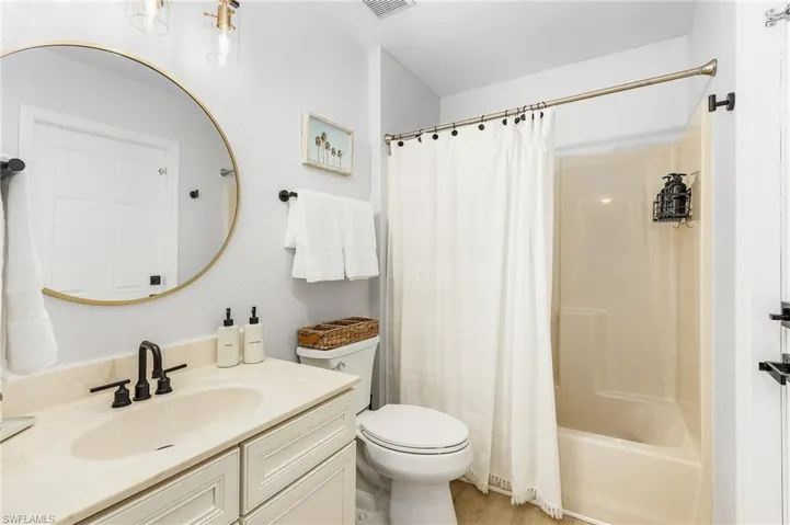 Full bathroom with hardwood / wood-style floors, shower / tub combo with curtain, vanity, and toilet