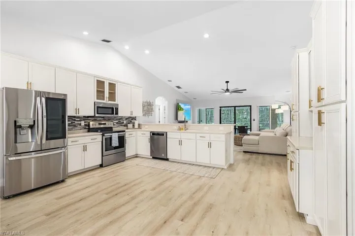 Kitchen with white cabinets, kitchen peninsula, light hardwood / wood-style flooring, appliances with stainless steel finishes, and vaulted ceiling