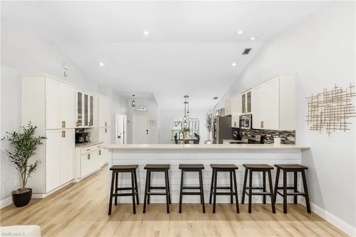 Kitchen with white cabinets, light hardwood / wood-style floors, appliances with stainless steel finishes, a breakfast bar, and vaulted ceiling