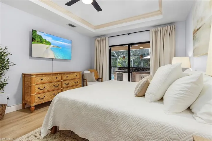 Bedroom with access to outside, light wood-type flooring, a tray ceiling, and ceiling fan