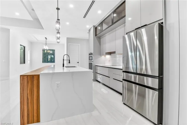 Kitchen with freestanding refrigerator, decorative light fixtures, modern cabinets, light stone counters, and a center island with sink