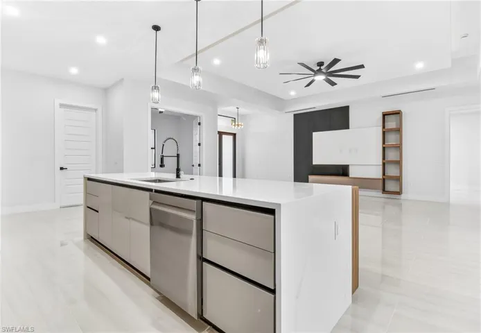 Kitchen with modern cabinets, hanging light fixtures, a kitchen island with sink, dishwasher, and light stone counters