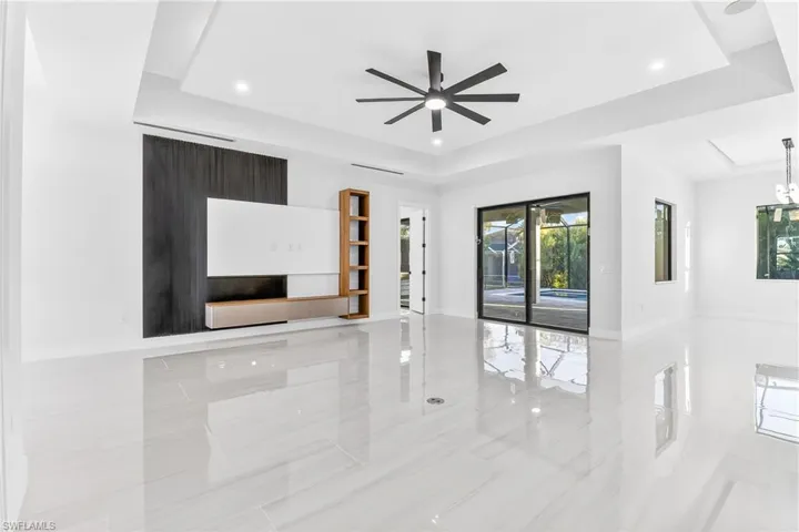 Unfurnished living room featuring a tray ceiling, a ceiling fan, and hanging lights