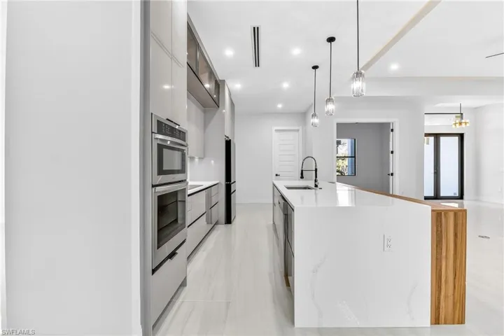Kitchen featuring modern cabinets, hanging light fixtures, stainless steel appliances, light stone counters, and a kitchen island with sink