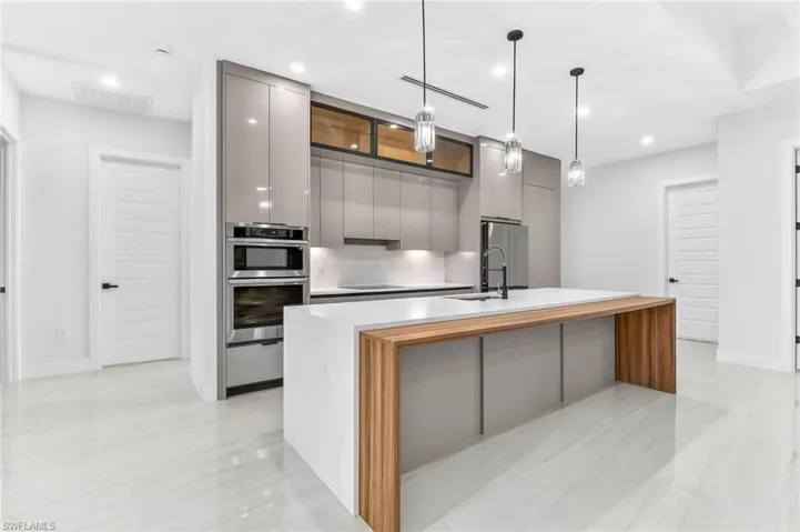 Kitchen with gray cabinetry, modern cabinets, a center island with sink, hanging light fixtures, and stainless steel appliances