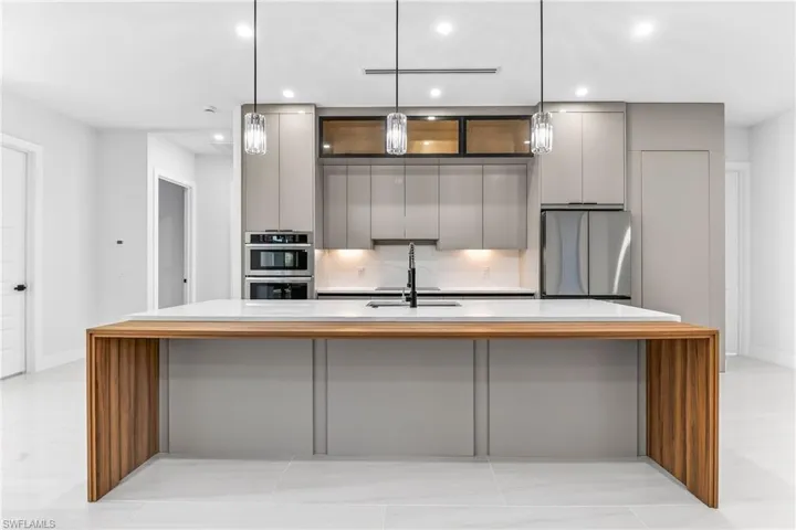 Kitchen with gray cabinets, modern cabinets, a spacious island, stainless steel appliances, and light stone countertops