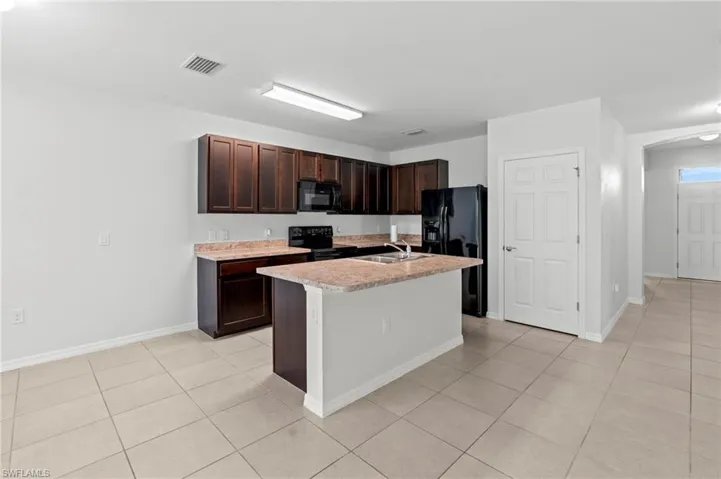 Kitchen with dark brown cabinets, light countertops, black appliances, a center island with sink, and light tile patterned floors