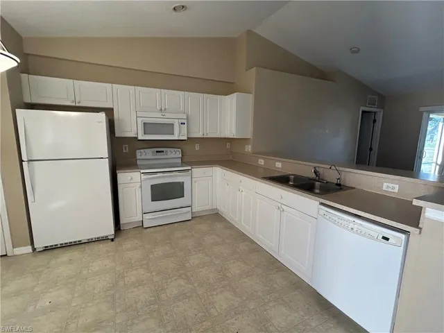 Kitchen featuring white appliances, white cabinets, light flooring, a peninsula, and lofted ceiling