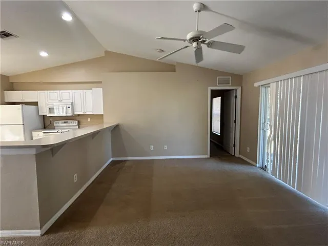 Kitchen with vaulted ceiling, white appliances, a peninsula, dark carpet, and a breakfast bar area