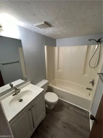 Bathroom with a textured ceiling, wood finished floors, vanity, and shower / washtub combination