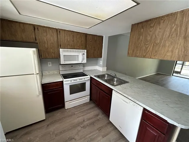 Kitchen with wood finished floors, white appliances, a peninsula, and light countertops