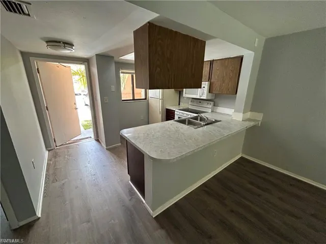 Kitchen featuring light countertops, a peninsula, dark wood-style flooring, and white appliances