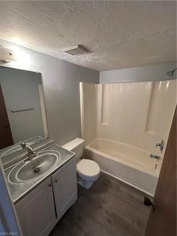 Full bathroom with dark wood finished floors, a textured ceiling, vanity, and  shower combination