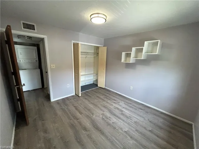 Unfurnished bedroom featuring stacked washing machine and dryer, dark wood-type flooring, and a closet