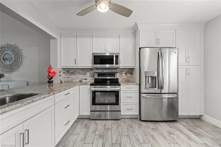 Kitchen with stainless steel appliances, light stone countertops, white cabinetry, and ceiling fan