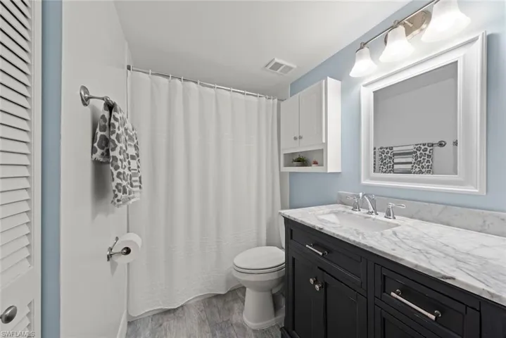Full bathroom with vanity, dark wood-style floors, a shower with shower curtain, and a closet