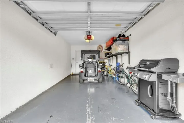 Garage interior featuring a painted concrete floor, white walls, and exposed ceiling joists