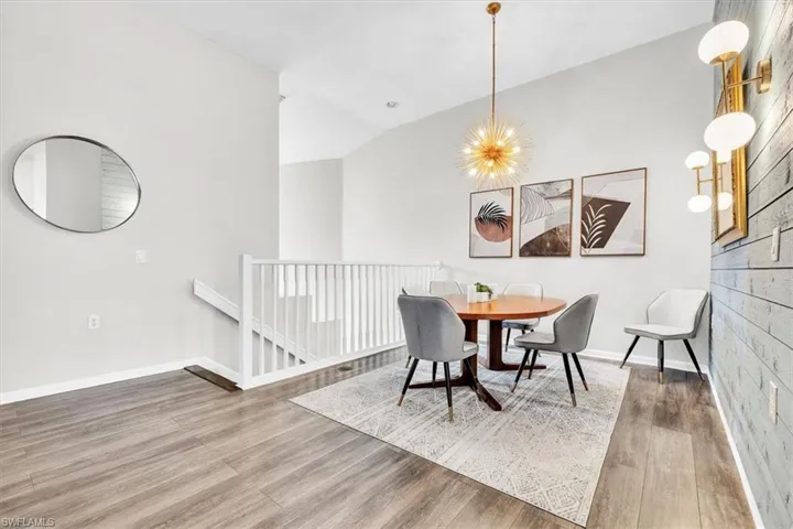 Dining area featuring a contemporary chandelier, wood-finish flooring, a decorative accent wall, a white staircase railing, and a vaulted ceiling