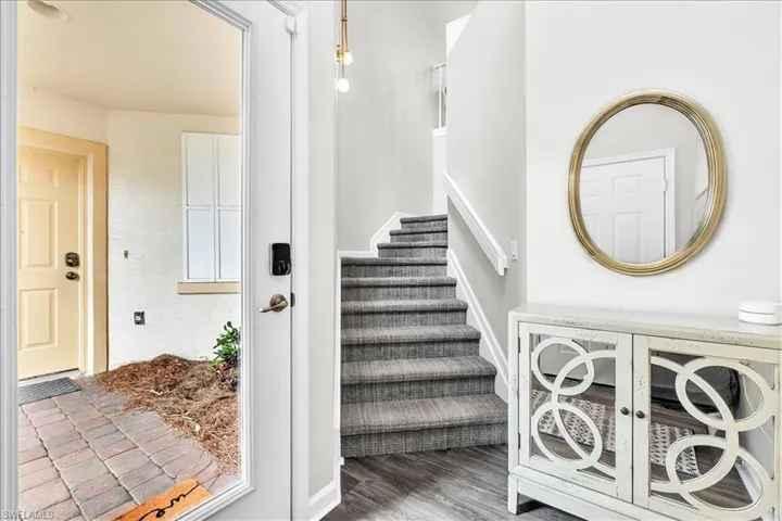 Foyer entry featuring wood-finish flooring, a carpeted staircase with white railings, and an overhead pendant light fixture
