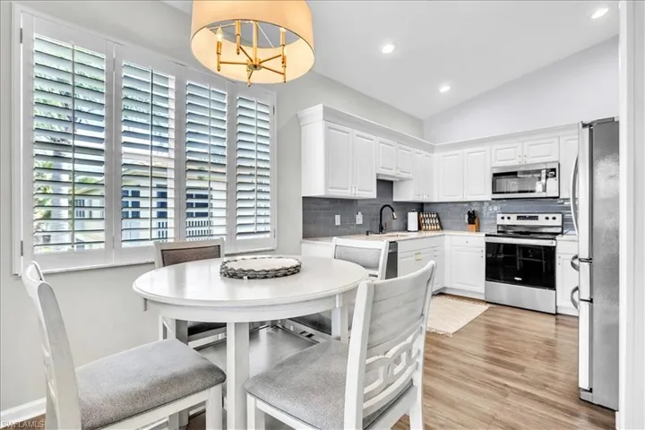 Kitchen area featuring white cabinetry, stainless steel appliances, a dark subway tile backsplash, and wood-finish flooring