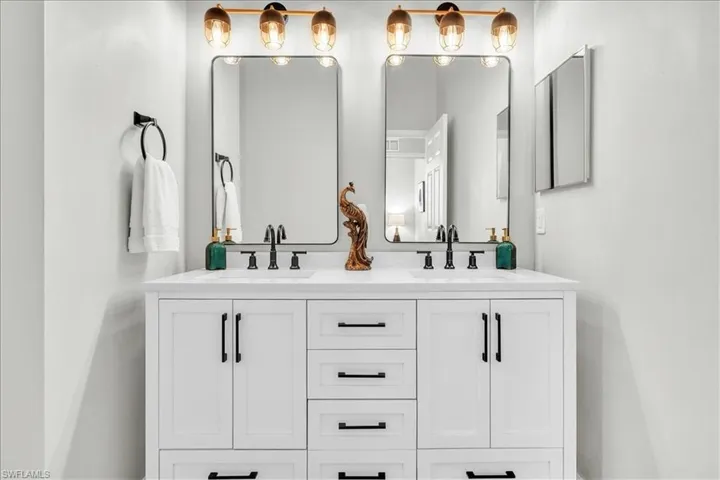 Dual vanity with integrated sinks, white cabinetry featuring black hardware, quartz countertop, two framed mirrors, and a gold-tone vanity light fixture