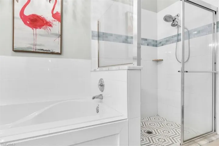Freestanding soaking tub with chrome fixtures, complemented by a glass-enclosed shower featuring a patterned tile floor, a dual shower head system, and a decorative blue and white tile accent band