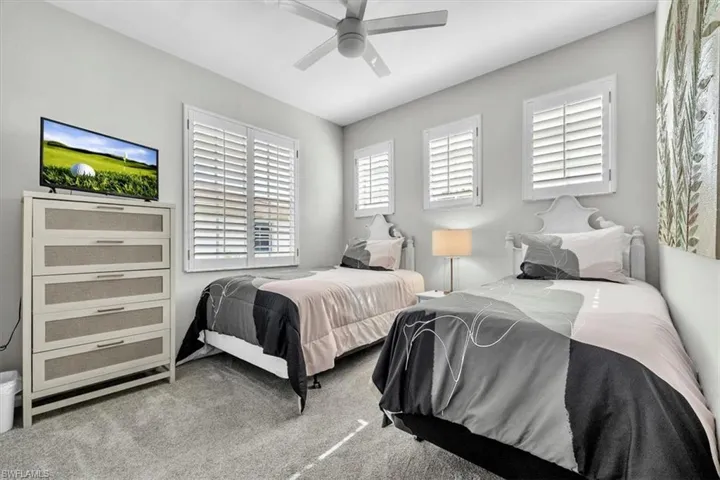 Light gray painted walls define this bedroom featuring two beds with matching white headboards, a ceiling fan, and gray carpeting