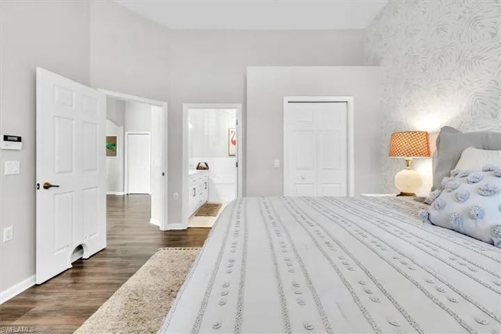 Bedroom featuring wood-finish flooring, vaulted ceilings, and a decorative accent wall