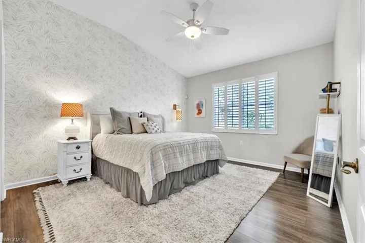 Room featuring a vaulted ceiling with a ceiling fan, wood-finish flooring, and a window with white plantation shutters