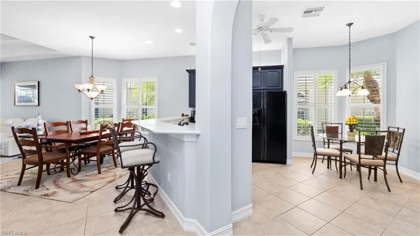 Kitchen featuring hanging lights, black refrigerator with ice dispenser, light tile patterned flooring, a breakfast bar area, and ceiling fan
