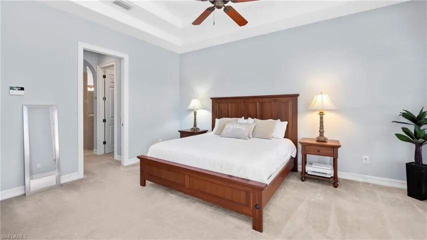Bedroom featuring a raised ceiling, light carpet, ceiling fan, and arched walkways