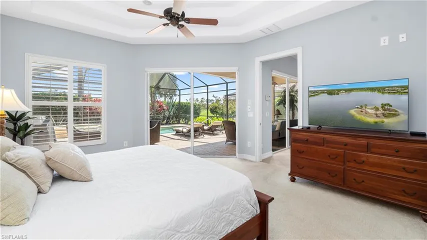 Primary Bedroom featuring sliding glass doors to the lanai and pool, light colored carpet, a tray ceiling and multiple windows