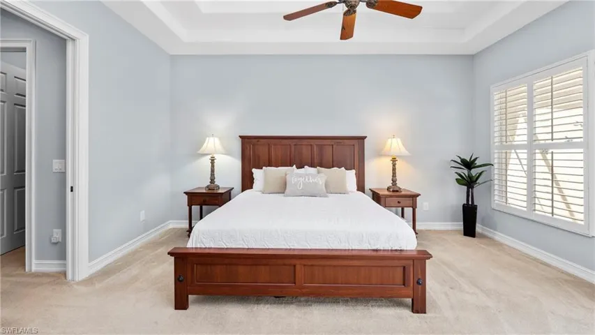 Bedroom with a raised ceiling, light colored carpet, and a ceiling fan