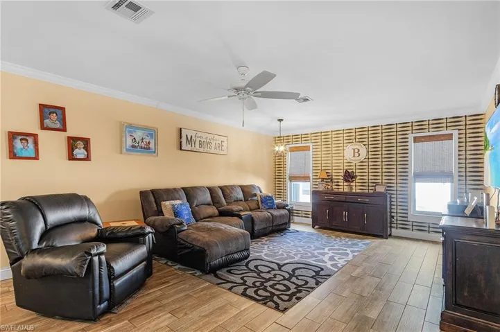 Living room featuring ornamental molding, ceiling fan with notable chandelier, and wood-type flooring