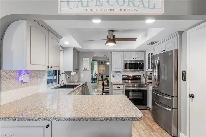 Kitchen featuring stainless steel appliances, kitchen peninsula, sink, decorative backsplash, and a tray ceiling