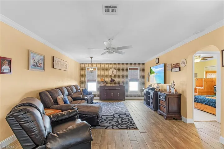 Living room with crown molding, light wood-type flooring, and ceiling fan