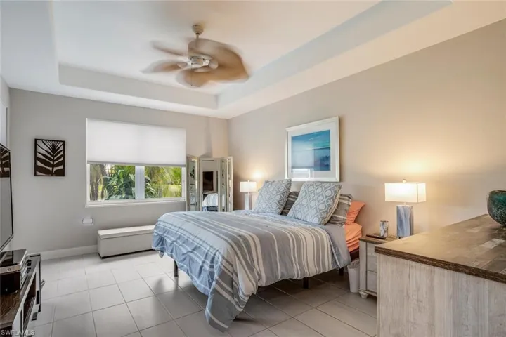 Bedroom with a raised ceiling, light tile patterned flooring, and a ceiling fan