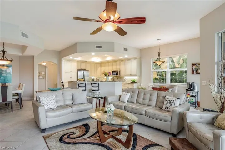 Living area with a ceiling fan, light tile patterned floors, arched walkways, a tray ceiling, and recessed lighting