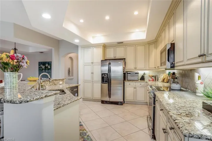 Kitchen with cream cabinets, light stone counters, appliances with stainless steel finishes, a tray ceiling, and backsplash