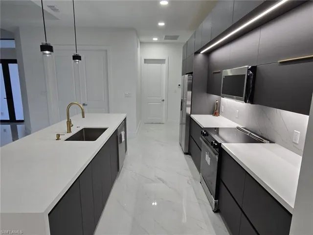 Kitchen featuring a kitchen island with sink, sink, pendant lighting, appliances with stainless steel finishes, and tasteful backsplash