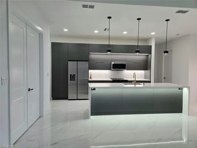 Kitchen featuring a kitchen island with sink, stainless steel appliances, hanging light fixtures, and sink