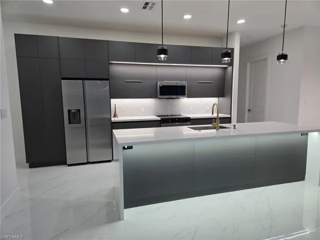 Kitchen featuring decorative backsplash, a center island with sink, sink, decorative light fixtures, and appliances with stainless steel finishes