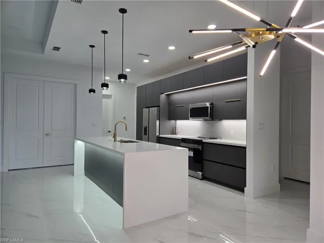 Kitchen featuring an island with sink, hanging light fixtures, stainless steel appliances, backsplash, and sink