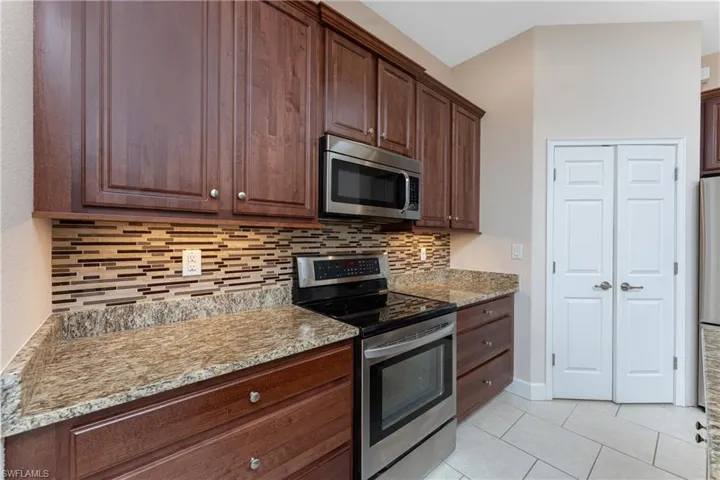 Kitchen with light stone counters, stainless steel appliances, backsplash, and light tile patterned floors