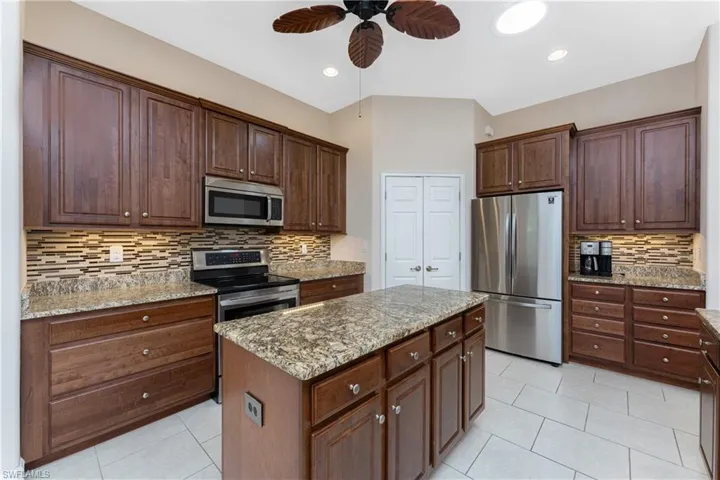 Kitchen featuring light tile patterned flooring, light stone counters, tasteful backsplash, appliances with stainless steel finishes, and a kitchen island