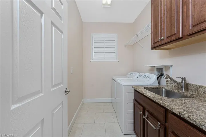 Laundry area featuring sink, light tile patterned floors, washing machine and dryer, and cabinets