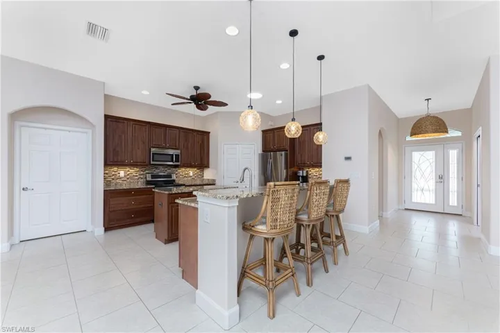 Kitchen with appliances with stainless steel finishes, backsplash, light stone countertops, a center island with sink, and decorative light fixtures