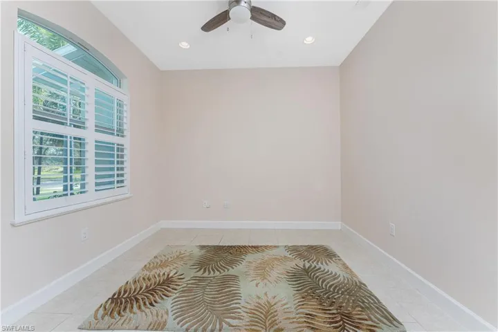 Tiled den or home office featuring plantation shutters and ceiling fan