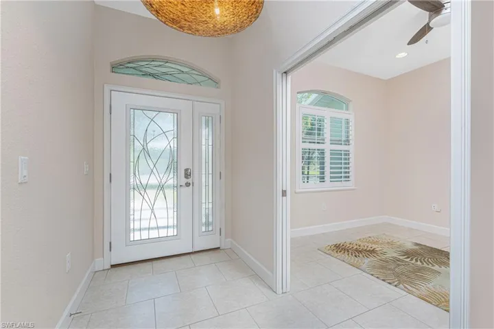 Tiled foyer with glass front door and arched window ceiling fa